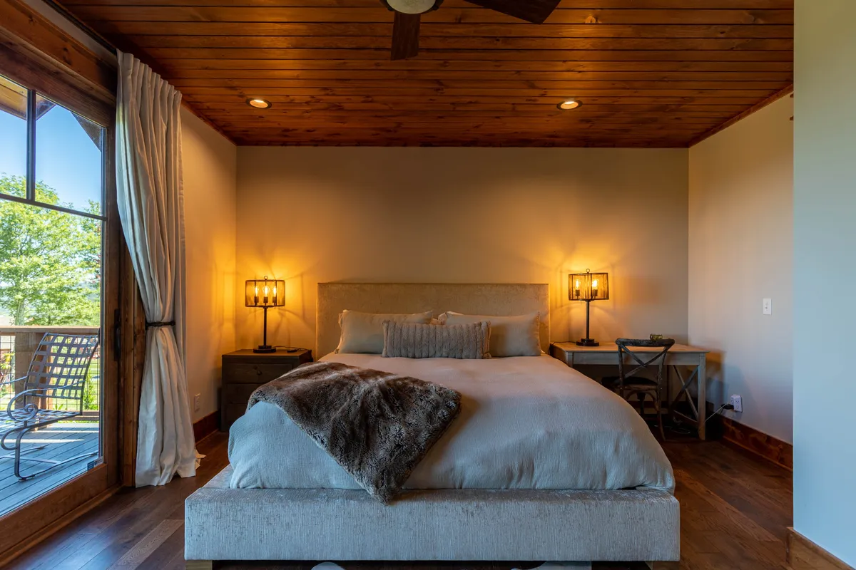 A serene bedroom with a large bed facing a window, soft lighting, and warm wooden accents. The space is cozy and tranquil, designed for relaxation and intimate moments, with sunlight streaming in to create a peaceful atmosphere.