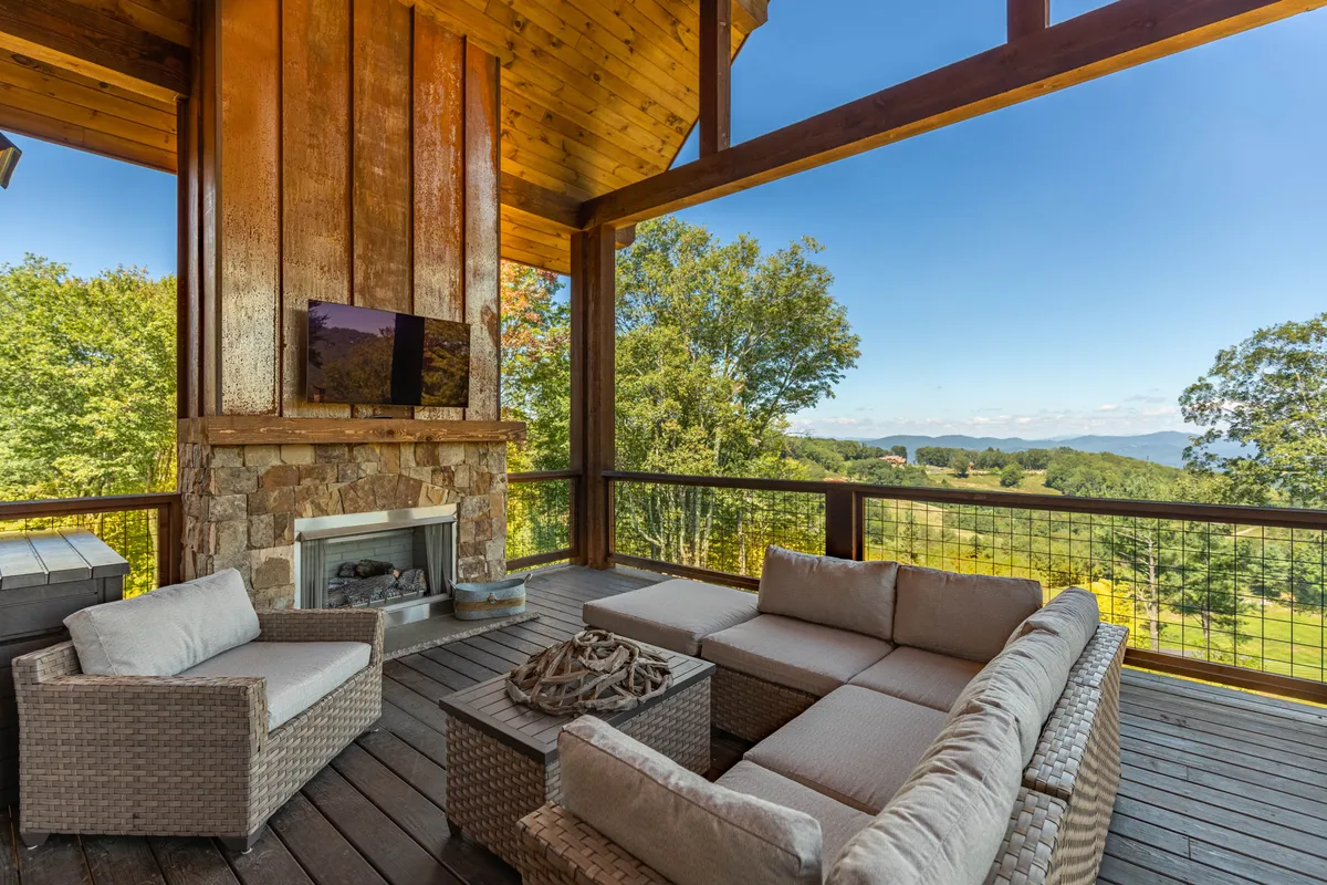 A covered outdoor living area features a striking stone fireplace, plush sectional seating, and expansive views of the surrounding mountains. The space is clearly designed for year-round enjoyment, offering both comfort and a strong sense of connection to the outdoors.