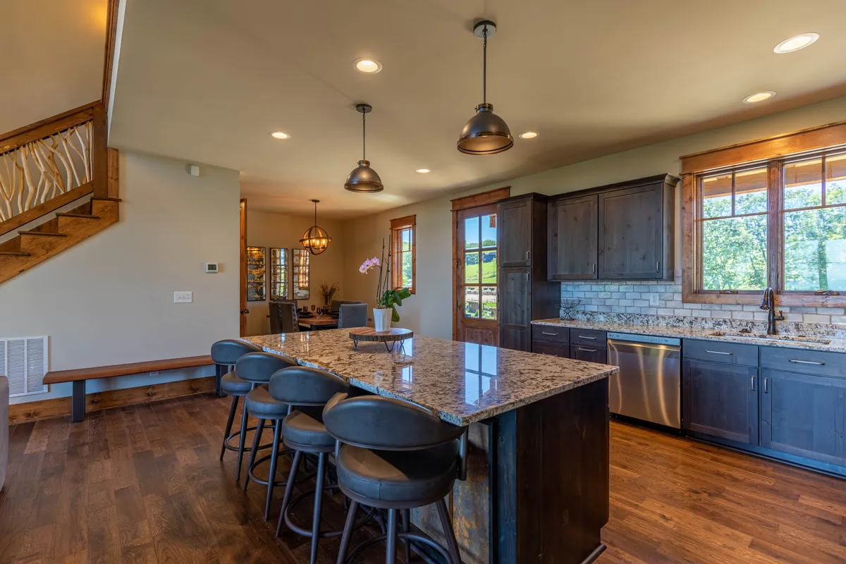 The bright and functional kitchen features a granite island with seating, modern stainless steel appliances, and sunlit windows. The space is designed for meal prep and casual dining, with cupboards fully stocked and an atmosphere that feels both homey and elegant.