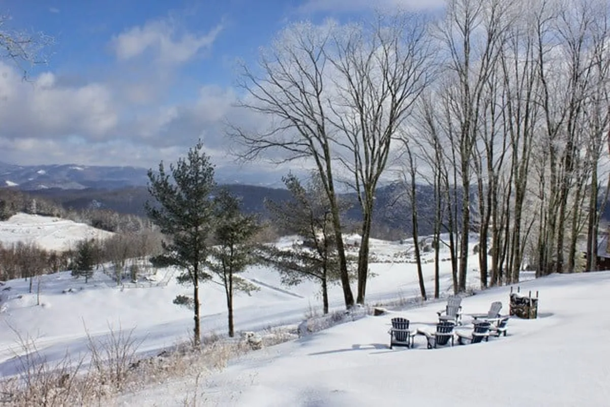 A tranquil outdoor setting with Adirondack chairs set on snow-covered ground, distant mountains, and bare winter trees. The mood is peaceful, inviting guests to relax by the fire pit or enjoy winter scenery after a day of adventure.