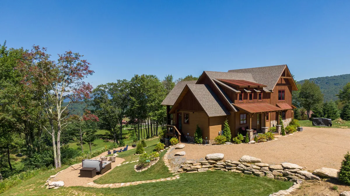 This exterior image features a welcoming house with an inviting outdoor seating area, nestled within a tranquil landscape. The view highlights gathering spaces perfect for sunset watching, socializing, and enjoying the natural surroundings, with hints of mountain vistas in the distance.