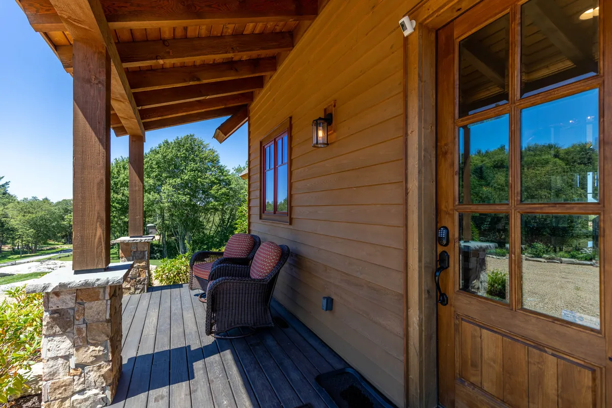 This exterior shot shows a comfortable front porch with rock columns, a wooden door, and inviting seating. The space is designed for relaxing, enjoying morning coffee, or hosting casual get-togethers, and is bathed in natural light, reinforcing the idea of seamless indoor-outdoor living.