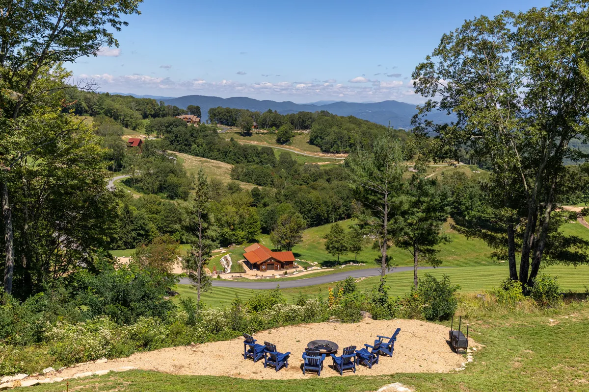 A cozy fire pit surrounded by blue chairs sits atop a grassy hill, overlooking rolling hills and distant mountains. The space is set up for communal gatherings, perfect for sharing stories, roasting s'mores, or stargazing late into the evening.
